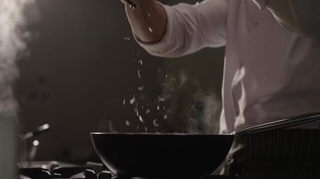 Chef's hands grating parmesan cheese over a hot, steaming pan while cooking in a restaurant kitchen, fa01