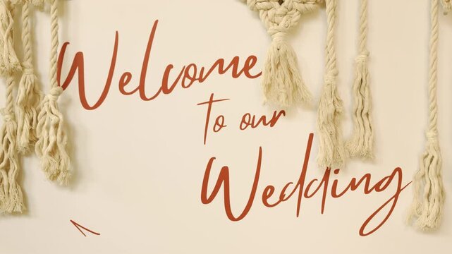 Welcome to our wedding sign decorated with elegant boho macrame texture backdrop. Slow motion close up of a beautiful handwritten marriage greeting board invitation banner for celebration.