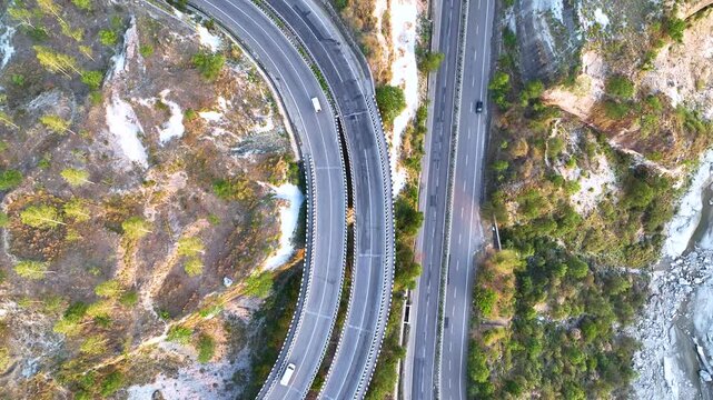 Top-down aerial drone footage capturing transport trucks and commuter vehicles navigating a sweeping S-curve on a major national highway. 