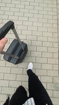 First-person POV walking with a black rolling suitcase across a paved sidewalk, vertical video capturing the excitement of departure, travel and the start of a new journey