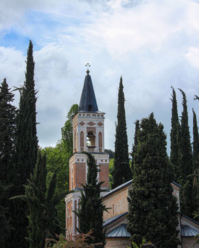 The church's bell tower is built of brown and white brick. Tall cypress trees surround it. Bodbe, Kakheti, Georgia