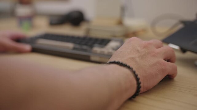 Man's hand using a computer mouse on a wooden desk with a mechanical keyboard in the background