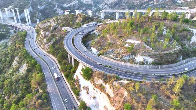 Freight truck driving on elevated highway curve. Cinematic aerial side-tracking footage following a brightly colored commercial transport truck as it navigates a sweeping, elevated curve on highway