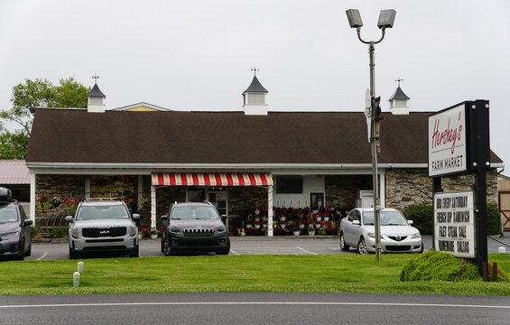 Parkesburg, Pennsylvania, U.S.A - May 11, 2026 - Hershey's Farm Market with stone exterior, striped awning, flower displays, and sign advertising barbecue and food specials.