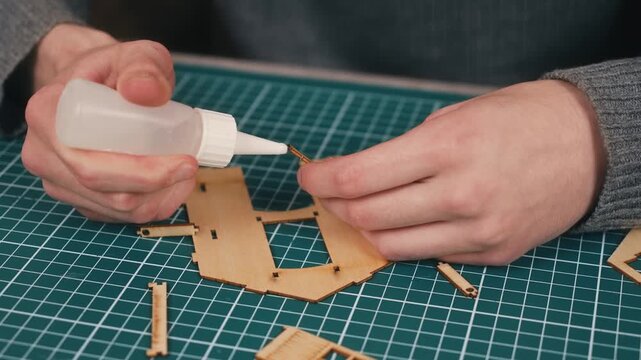 Applying glue to wooden miniature house components during model assembly. DIY architecture crafting featuring plywood detail installation and precision home construction process. Creative housing