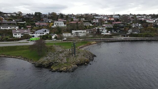 Cinematic 4K drone flight towards the famous Sverd i fjell monument on the rocky shore of Hafrsfjord in Stavanger, Norway. Aerial view of traditional coastal houses and road. Real time.
