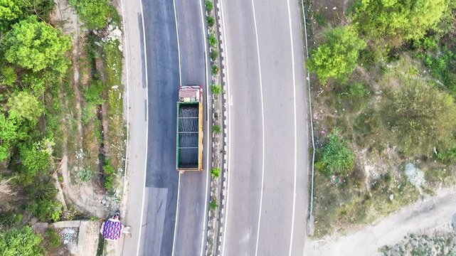Bird's eye view tracking freight truck loaded with construction material. Perfect 90-degree top-down aerial drone footage tracking a heavy commercial transport truck loaded with steel rebar