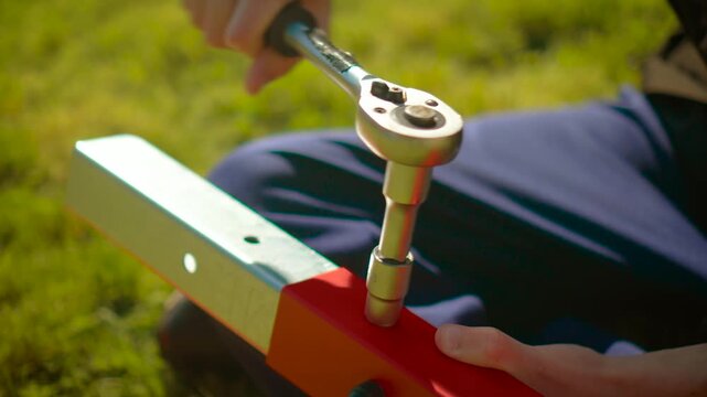 Technician tightening bolt with ratchet wrench on red metal beam outdoors. DIY assembly repair work with hand tool in sunlight. Construction maintenance concept with worker using socket wrench on