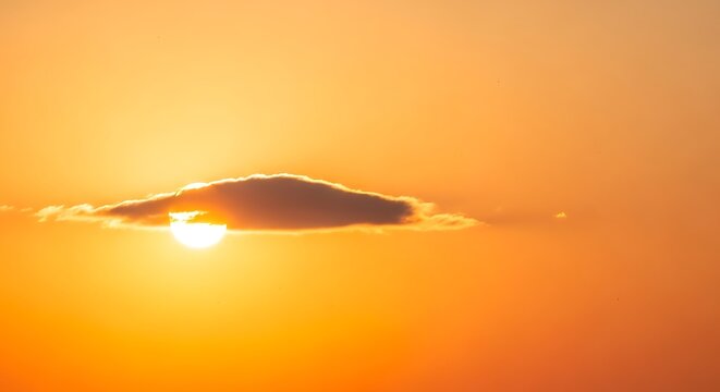A bright golden sunset sun partially obscured by a single dark elongated cloud formation.