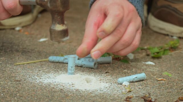 Grey expansion anchor placing into concrete opening after drilling operation detail. Worker hand aligning dowel inside hole for fastening installation in building task. Repair workflow emphasizing