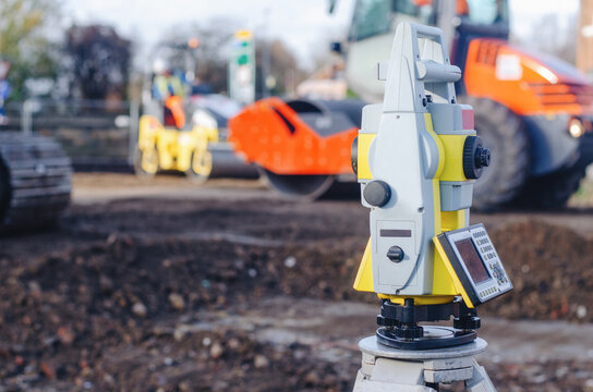 Construction equipment at a site with a surveying instrument in focus near machinery and workers