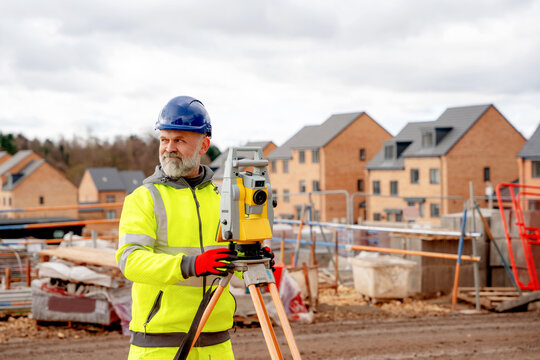 Surveyor working on a construction site with unfinished buildings in the background on a cloudy day