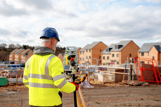 Surveying land at a construction site during daytime with new homes in the background