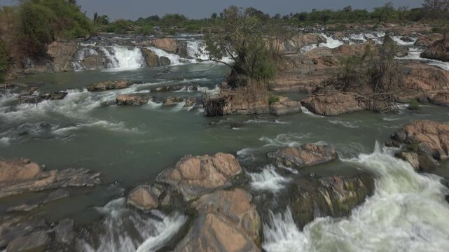 Drone push forward over fish traps and a riverside tree to the upstream channels above Khone Pa Soi Waterfall, Laos.