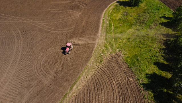 Aerial View of a Red Tractor Harrowing a Large Agricultural Field