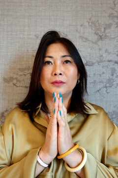 A stylish woman with teal nails and bangles meditates with hands in prayer. Haiphong. Vietnam.