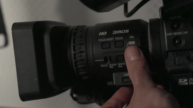 Close-up of a videographer adjusting audio levels and settings on a professional video camera in a studio environment.