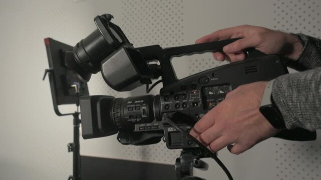 Close-up of a videographer adjusting audio levels and settings on a professional video camera in a studio environment.