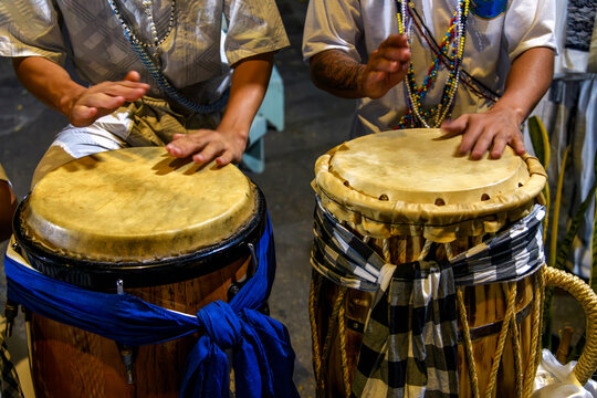 Drummers playing a traditional atabaque drum decorated with cloths during an Umbanda celebration in Brazil.