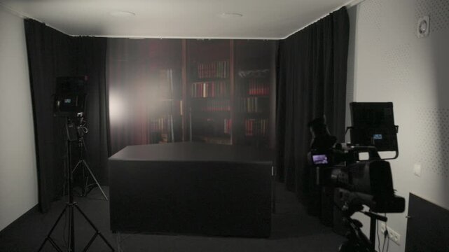 Empty professional video production studio with camera setup, lighting equipment, and a library background ready for recording.