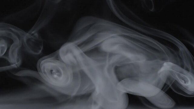 Abstract slow motion of ethereal white smoke swirling and flowing against a dark background, creating organic textures and patterns