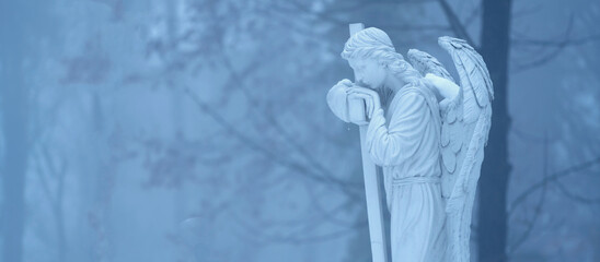 Fototapeta premium White angel statue standing alone in a mysterious foggy forest atmosphere