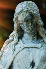 Fototapeta premium Ancient angel statue with weathered face in warm dramatic light, symbolic image of silence, sorrow and eternity