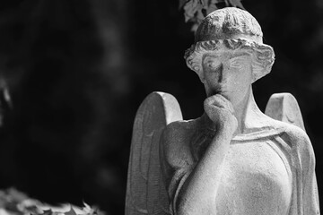 Fototapeta premium Monochrome angel statue with thoughtful expression in dramatic cemetery atmosphere