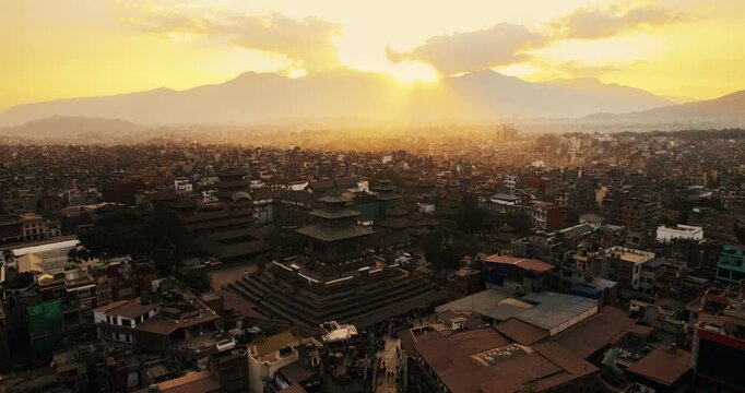 Aerial drone shot of Basantapur Durbar Square at golden sunset, with ancient pagoda temples silhouetted against the misty Kathmandu valley and distant Himalayan foothills.