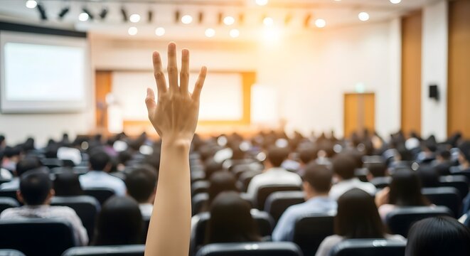 A person raising their hand in a large, brightly lit conference hall filled with attendees, indicating active engagement in a professional seminar.