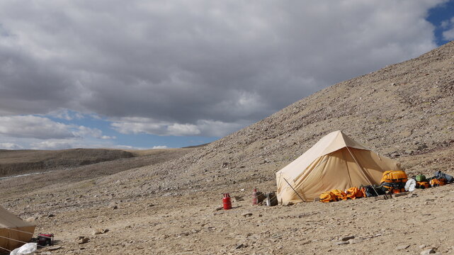 A yellow basecamp tent pitched on a barren rocky slope under a dramatic cloudy sky, concept of shelter, rest, and survival during a high-altitude expedition in Ladakh, Himalayas.