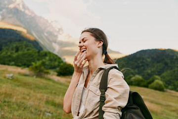 A happy young woman with a backpack laughs outdoors in a mountainous landscape during daytime. She wears casual clothes and enjoys nature, representing lifestyle and adventure. © SHOTPRIME STUDIO