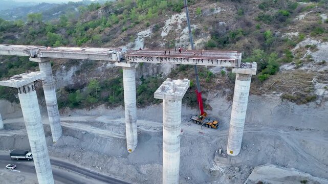 Active civil engineering: Crane lifting materials onto bridge pillars. Dynamic aerial drone footage capturing active heavy civil engineering as a construction crew and a large mobile crane working.