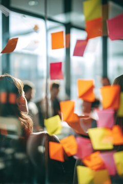 Woman looking at colorful sticky notes on glass wall during team meeting. Colleagues brainstorming creative project ideas in modern office. Business planning and development strategy concept.