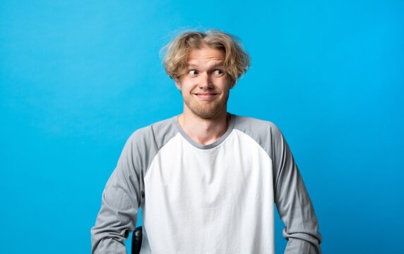Young man creating a funny face and an awkward expression, looking away with side eye, showing suspiciousness and uncertainty on a vibrant blue background
