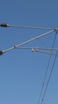 Low-angle close-up of railway overhead electrification (OHE) wires and catenary assembly against a clear blue sky