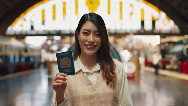 Portrait of young Asian lesbian holding passport on railway platform. Confident transwoman in smart casual shows personal ID for travel at train station. Business trip style