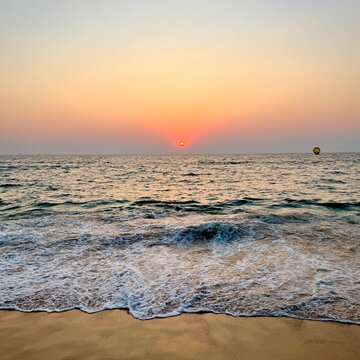 Luxury sunset experience on Candolim Beach, Goa, India. Parasailing, sailboat, and cruise ship on the horizon with elegant table detail on the sand.