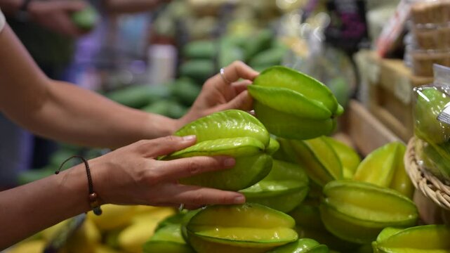 Shopper selecting fresh tropical fruits from grocery store. Customer choosing carambola starfruit for buying. Healthy food choice, vegetarian lifestyle, organic produce in supermarket for travelers. 