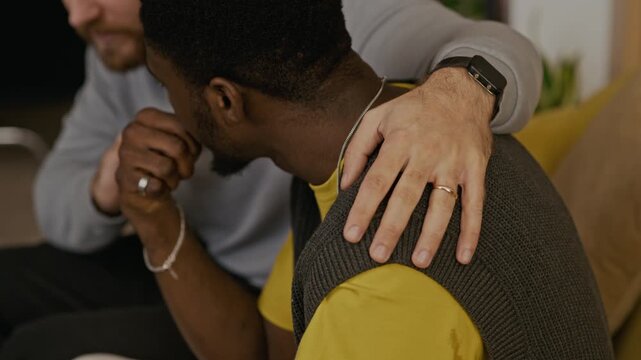 High angle shot of Caucasian man hugging African American man while having supportive conversation in living room