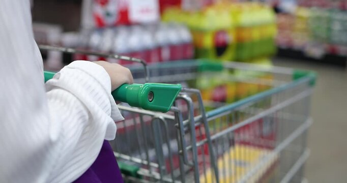Woman pushing a shopping cart in a supermarket aisle, browsing products on shelves. Ideal for retail, lifestyle, consumer, and shopping concept content
