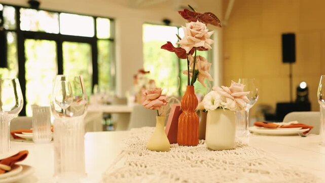 Wedding table decoration with elegant roses in ceramic vases on a boho macrame runner. Slow motion close up of a beautiful floral arrangement and dinner glasses for a marriage reception.