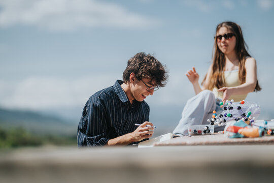Two young students study chemistry outdoors with a molecular model and notebooks. The pair work together on a science project outside, surrounded by study materials.