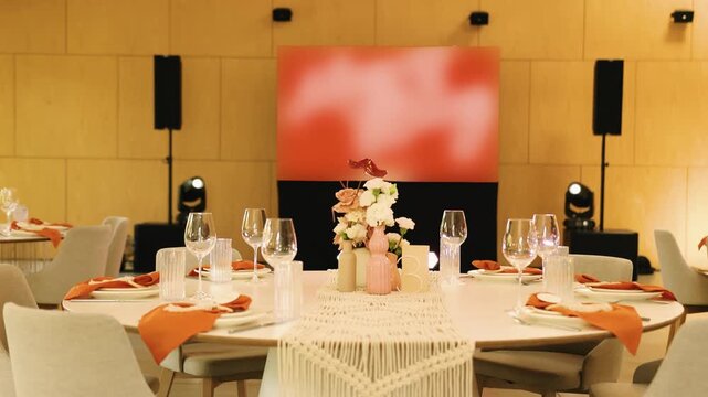 Wedding venue reception hall setup with elegant round dinner table layout and modern interior design. Slow motion of a beautiful marriage banquet room decoration with chairs and screen backdrop.