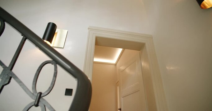 Interior low angle tracking shot of a classic winding staircase with an ornate iron railing and wall lamps