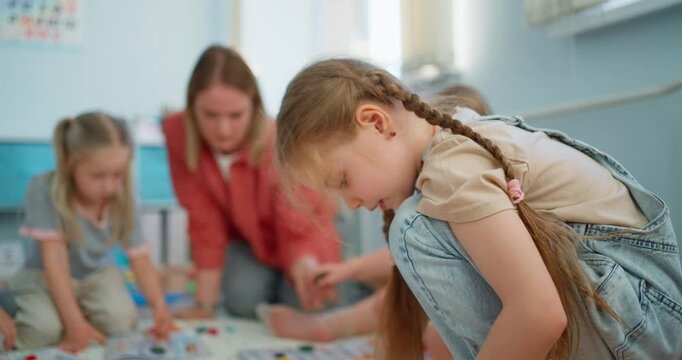 Young girls sitting on a classroom floor playing a colorful board game together, concentrating on pieces during a calm indoor learning activity