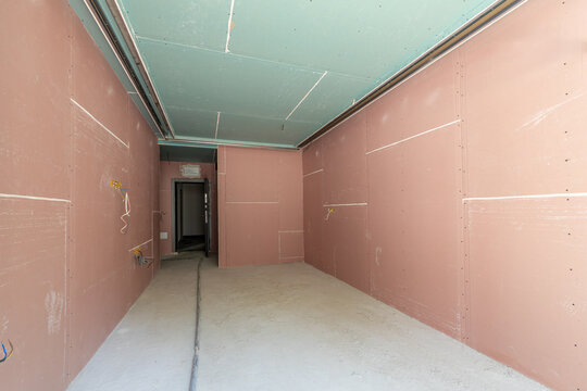 Interior of a room under construction with pink and green drywall panels. Apartment renovation, remodeling, and electrical wiring installation. New home building and improvement concept.