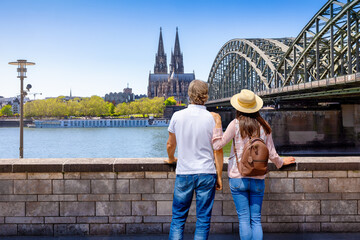 Fototapeta premium A tourist couple on a city tour looks at the skyline of Cologne, Germany, with Cathedral and river Rhine during a sunny summer day