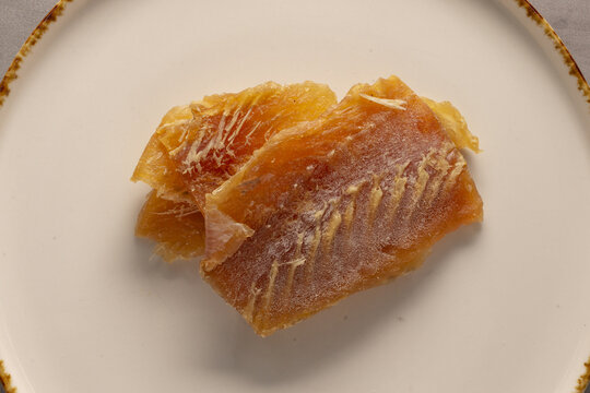 Dried fish fillet on porcelain plate, golden cured texture, minimalist food styling, soft natural light, closeup overhead view,