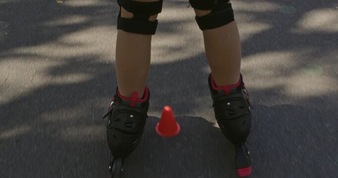 Girl glides past cones on inline rollerblades during park training. Child keeps knees bent following marked route to practice control on pavement with steady movement